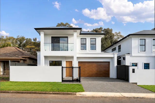 White two-storey home with timber garage door and landscaped front garden